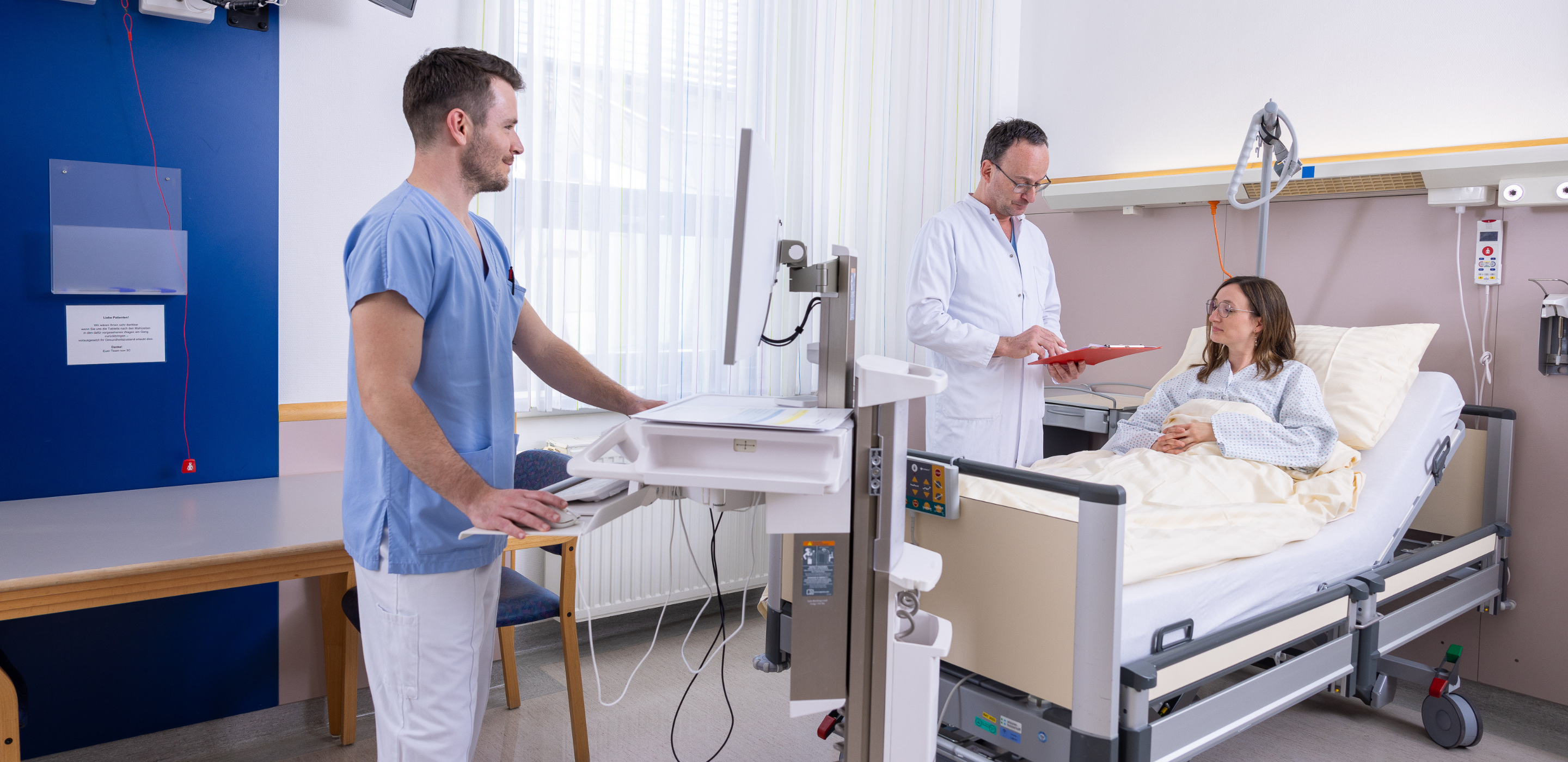Pfleger und Arzt stehen bei Patientin am Krankenbett