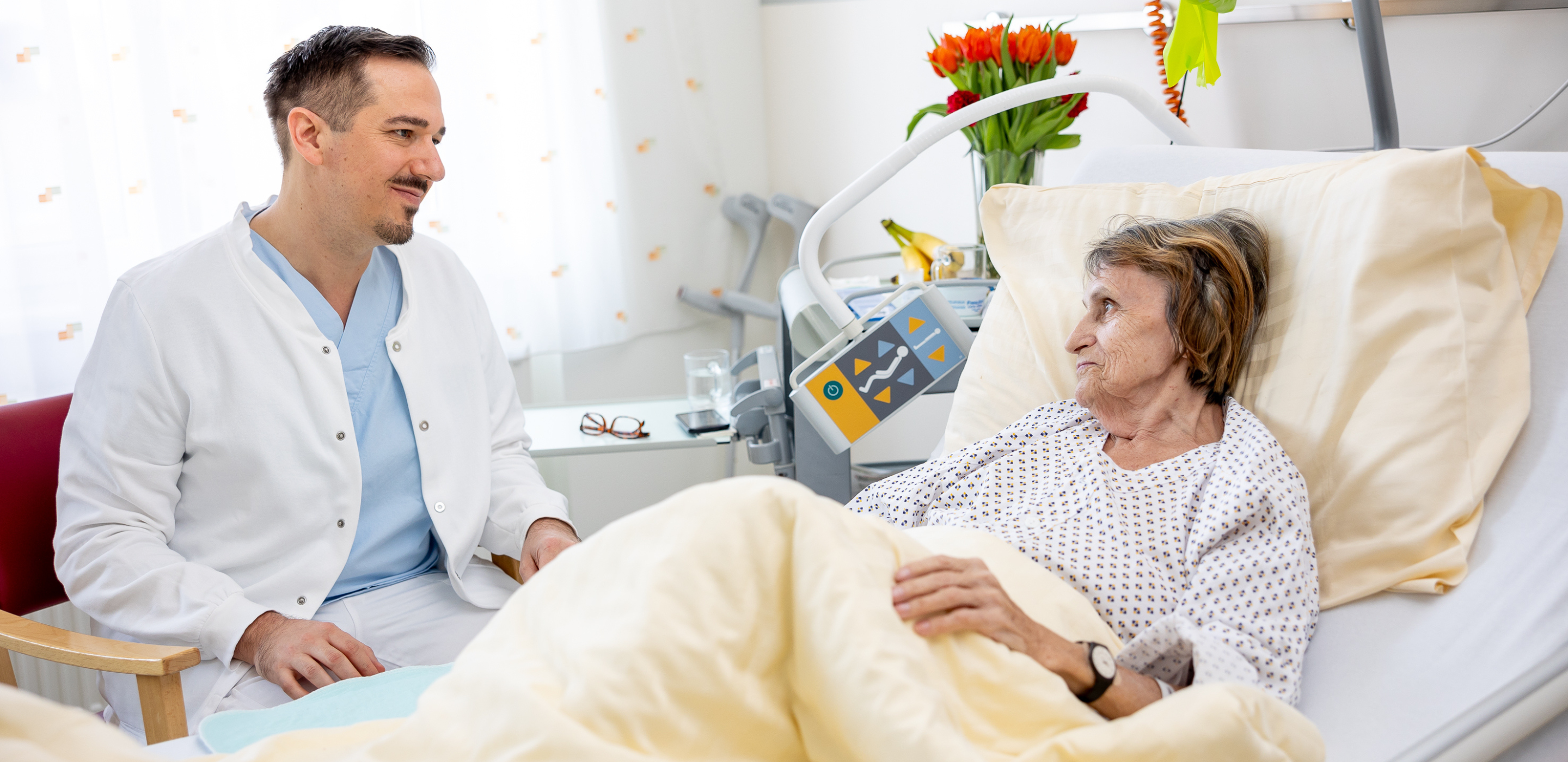 Arzt sitzt bei älterer Patientin neben dem Krankenbett