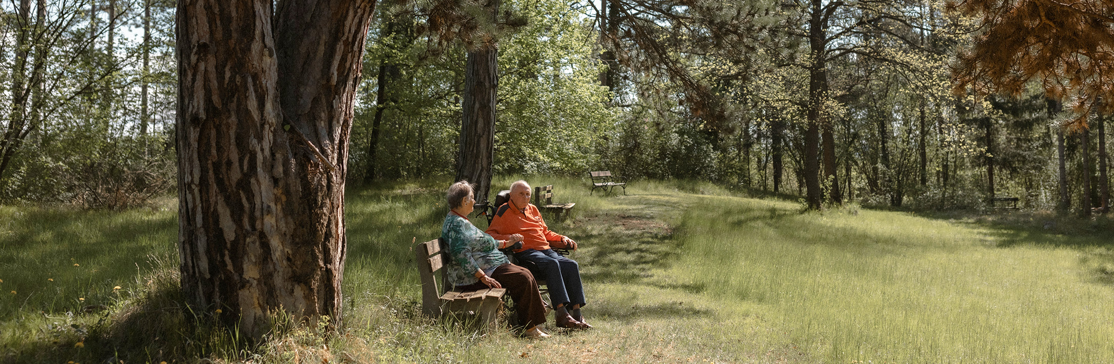 Zwei Bewohner*innen sitzen auf Bank umgeben von Wald