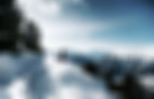 Person standing on a snow-covered mountain ridge with panoramic views of distant peaks and a clear blue sky.