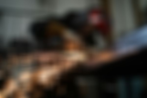 A person wearing protective gear uses an angle grinder on metal, creating bright sparks in a workshop setting.