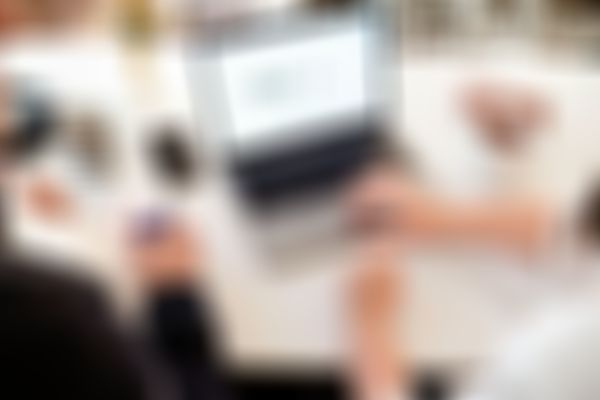 Two people working at a desk with a laptop, notebook, smartphone, coffee mugs, and headphones, focused on a digital marketing website.