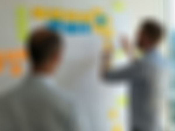 Two men in a meeting room discussing a board covered with colorful sticky notes, indicating a brainstorming or planning session.