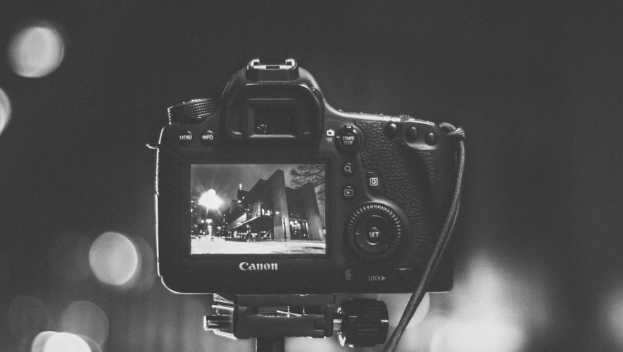 Zbliżenie aparatu DSLR na statywie, rejestrującego czarno-biały krajobraz miejski nocą, z rozmytymi światłami w tle.