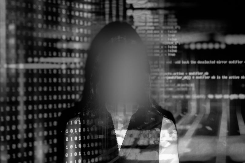 Persona silueteada con una cara borrosa contra un fondo de código binario y texto digital, creando una misteriosa escena de temática tecnológica.