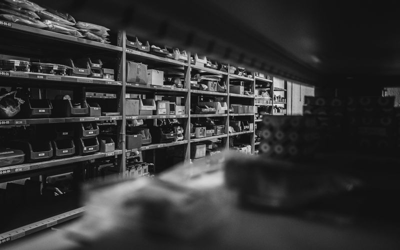 Imagen en blanco y negro de un trastero con estantes llenos de diversas cajas y artículos, creando un ambiente organizado e industrial.