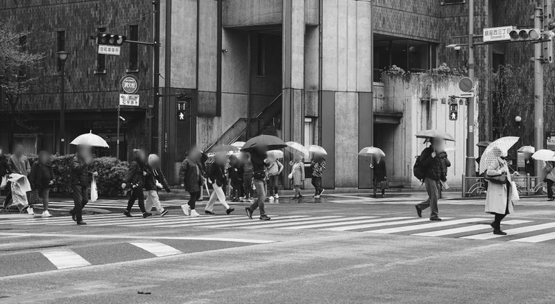 foto de una ciudad concurrida en blanco y negro, peatones con paraguas y rostro borroso anoniminzado