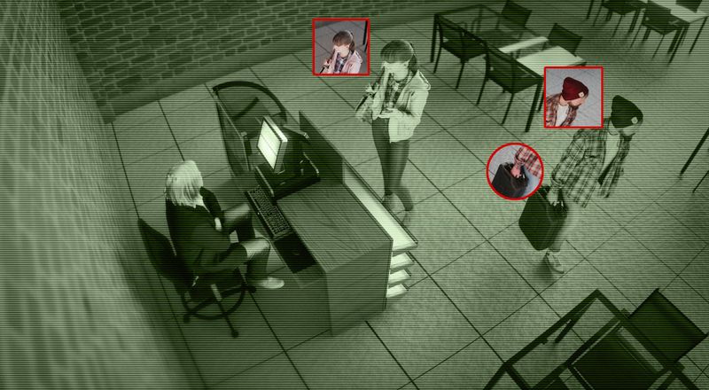 Security camera footage showing a person seated at a computer and three people standing nearby, with faces highlighted in red squares.