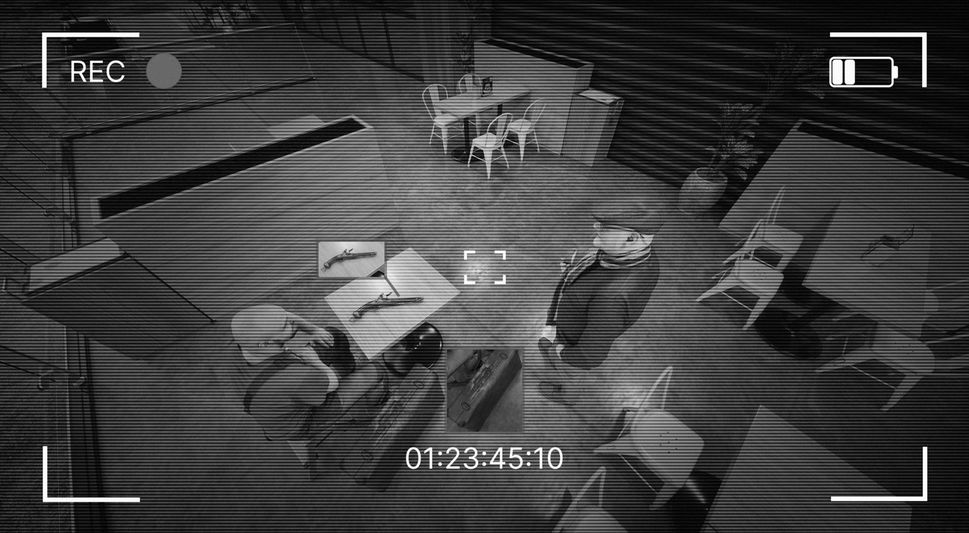 Images de vidéosurveillance montrant deux hommes dans une pièce faiblement éclairée avec des tables et des chaises, discutant près d'une table avec des fusils et une valise.