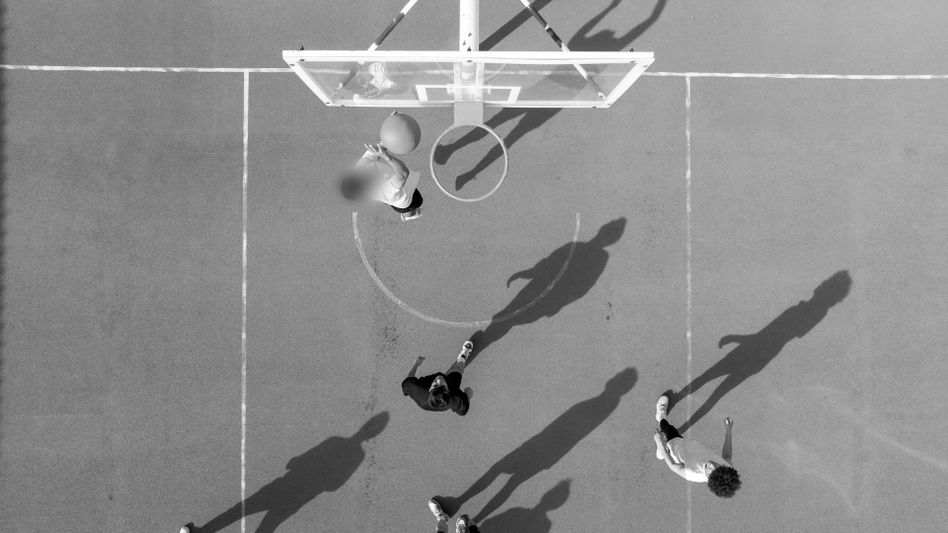 Aerial view of people playing basketball on an outdoor court, with long shadows cast on the ground.