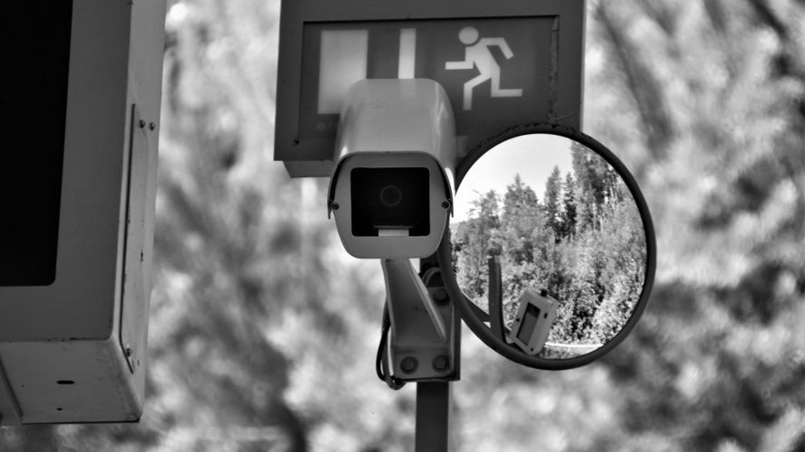 a grayscale photo showing a camera on a metal pole along with a mirror and an evacuation sign