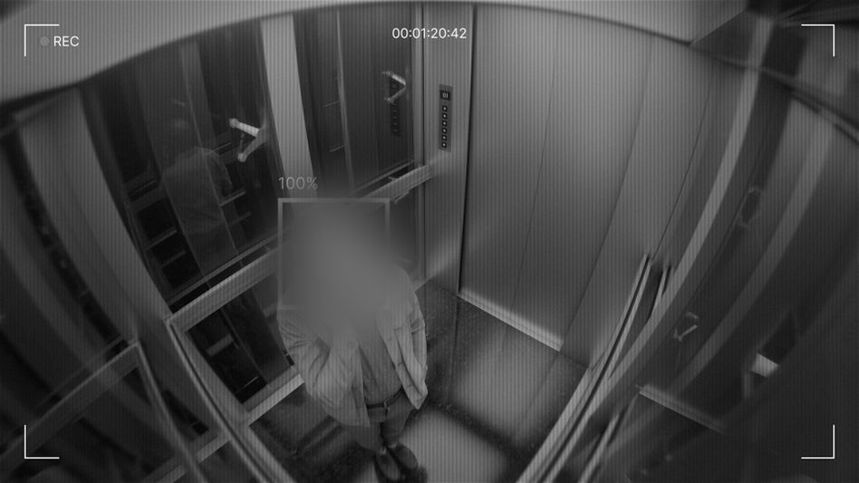 CCTV footage of a person in an elevator, face blurred for privacy, with reflective walls and a visible control panel.