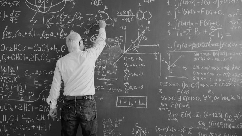 A man writes complex mathematical and chemical formulas on a large board, surrounded by graphs and equations.