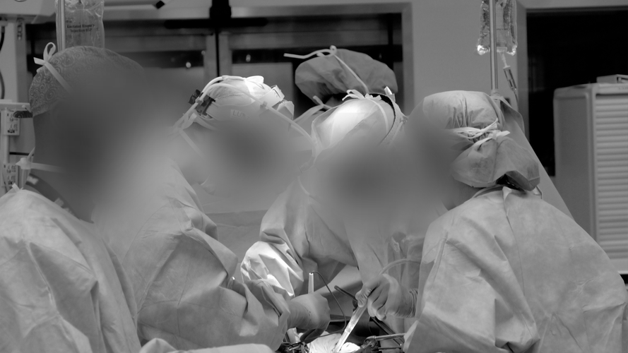 Zespół medyczny ubrany w fartuchy i maski wykonuje operację na sali operacyjnej, skupiając się intensywnie na zabiegu.