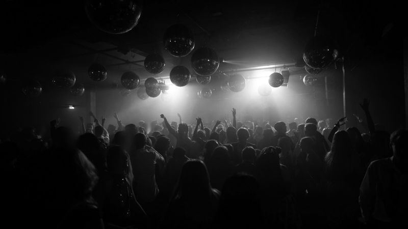 A crowd dances in a dimly lit nightclub with disco balls hanging from the ceiling, creating a lively and atmospheric scene.