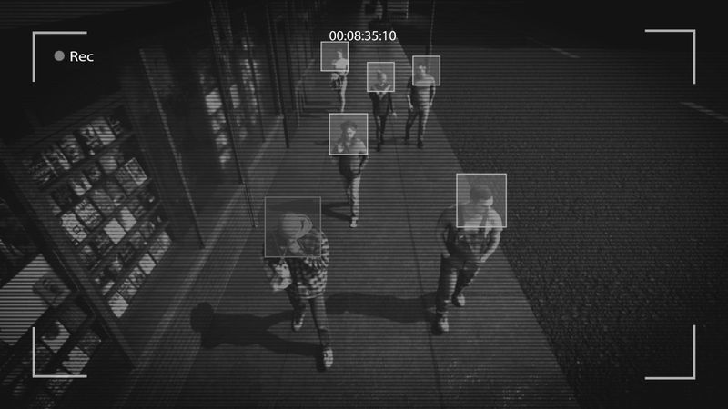 Vista de cámara de vigilancia de personas caminando por una acera, con cuadros de reconocimiento facial alrededor de sus caras.