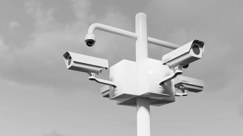 cuatro cámaras de vigilancia blancas apuntando exactamente hacia las cuatro direcciones y dos móviles también blancas; con el cielo de fondo