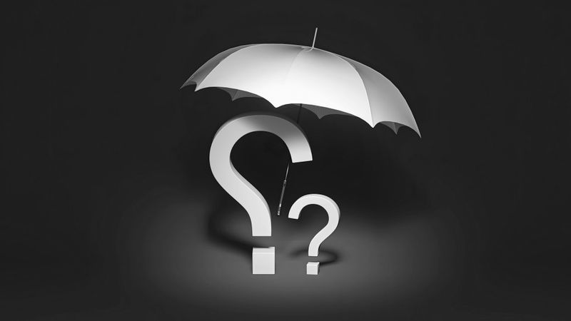 Dos signos de interrogación bajo un paraguas blanco contra un fondo oscuro.