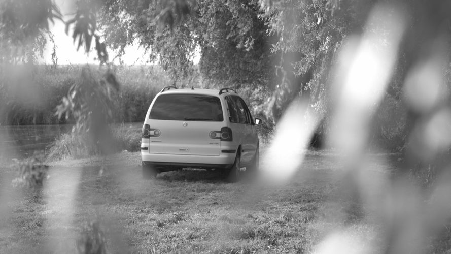 czarno-białe zdjęcie samochodu nad zbiornikiem wodnym, stającym pod drzewem. biały Samochód suv ma zamazaną tablice rejestracyjną