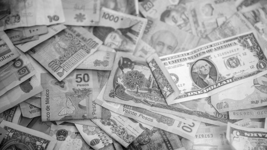A black-and-white photo of various international banknotes, including the US dollar and Mexican pesos, scattered randomly.
