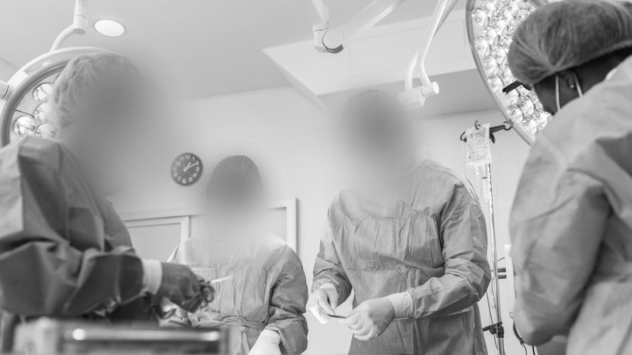 Lekarze w strojach operacyjnych wykonujący zabieg w dobrze oświetlonej sali operacyjnej, na tle widocznego sprzętu medycznego.