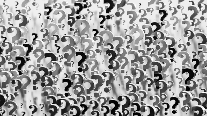 Multiple overlapping black and gray question marks of varying sizes on a white background, creating a textured, abstract pattern.