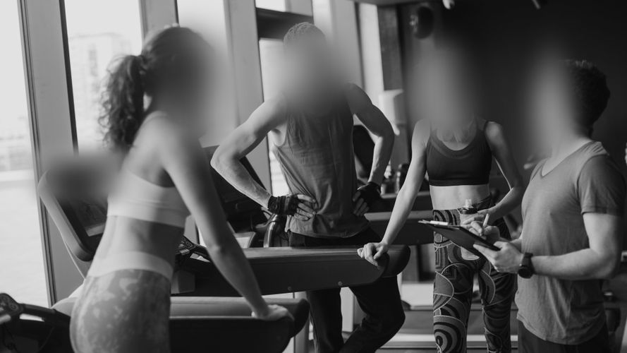 Cztery osoby w sportowych strojach rozmawiają przy sprzęcie do ćwiczeń w nowoczesnym studiu fitness.