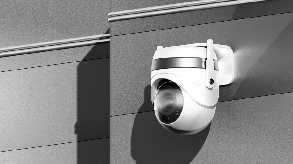 A white security camera mounted on a modern, textured wall, casting a shadow.