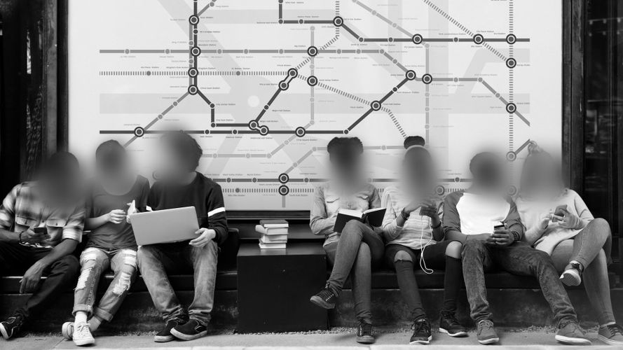 Grupa ludzi siedzi na ławce, czytając książki i korzystając z laptopa, przed mapą metra.