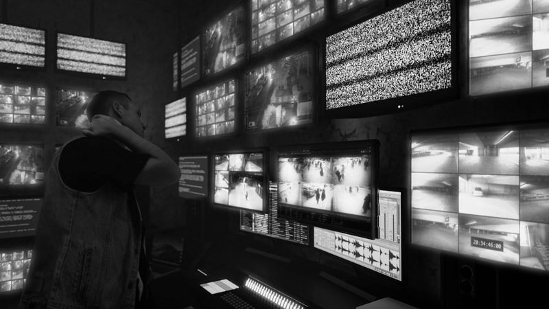 Une personne se tient devant plusieurs moniteurs de surveillance, certains affichant de la neige, dans une salle de contrôle faiblement éclairée.