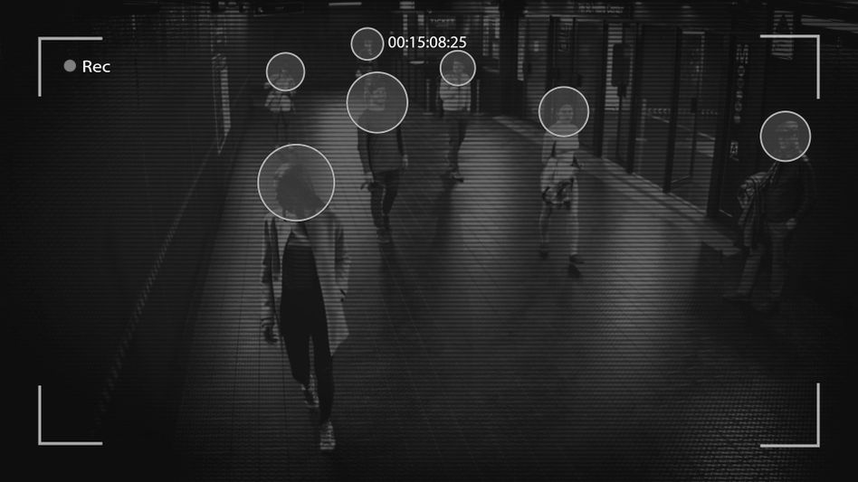 Surveillance footage showing several people walking in a dimly lit corridor, with facial recognition markers on their faces.