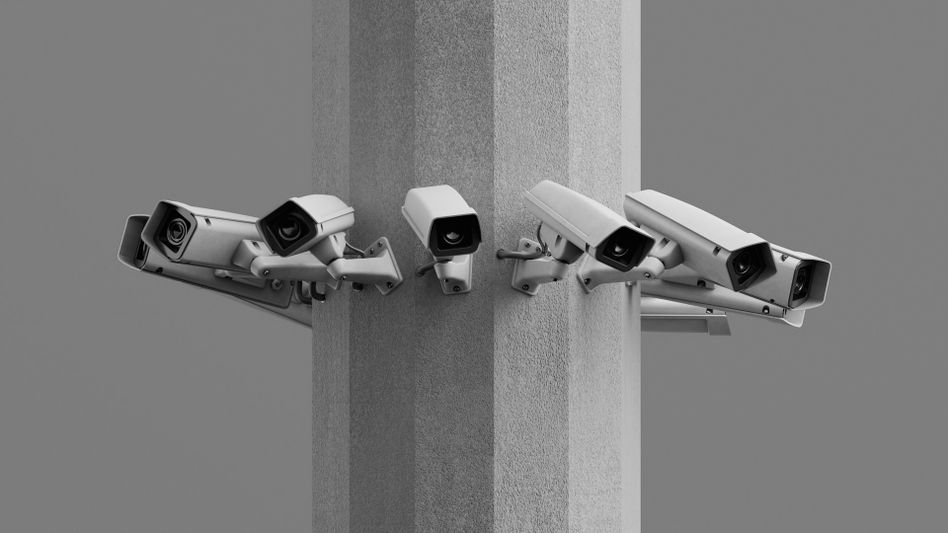 Plusieurs caméras de surveillance montées sur un poteau en béton gris, orientées dans différentes directions sur un fond uni.