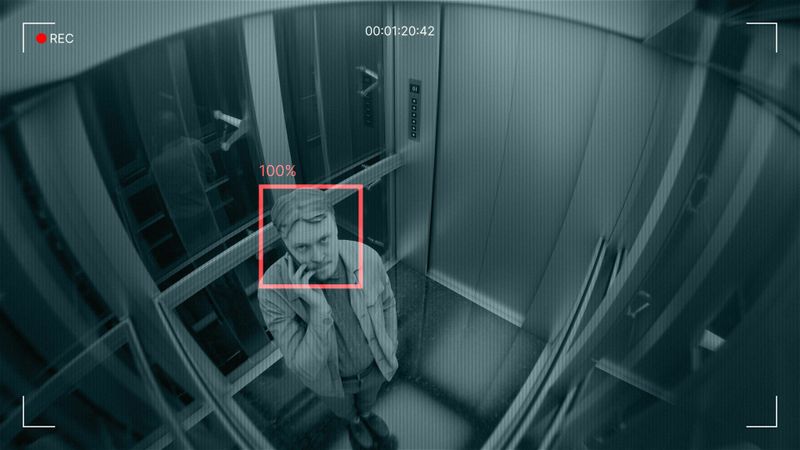 CCTV view inside an elevator with facial recognition detecting a person; red square highlights the face.