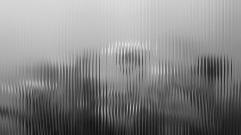 Blurred abstract pattern with vertical lines creating a rippled effect, resembling frosted glass, in grayscale tones.