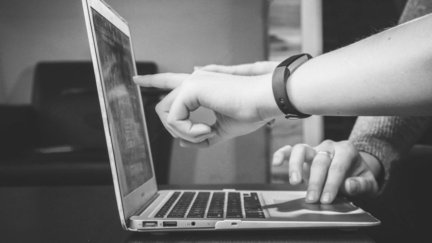 Deux personnes devant un ordinateur portable : l'une pointe l'écran du doigt tandis que l'autre tape sur le clavier (image en noir et blanc)