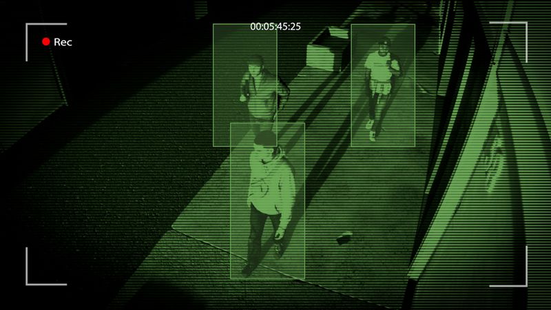 Night-vision security footage shows three individuals walking down a dimly lit corridor, with motion detection boxes around them.