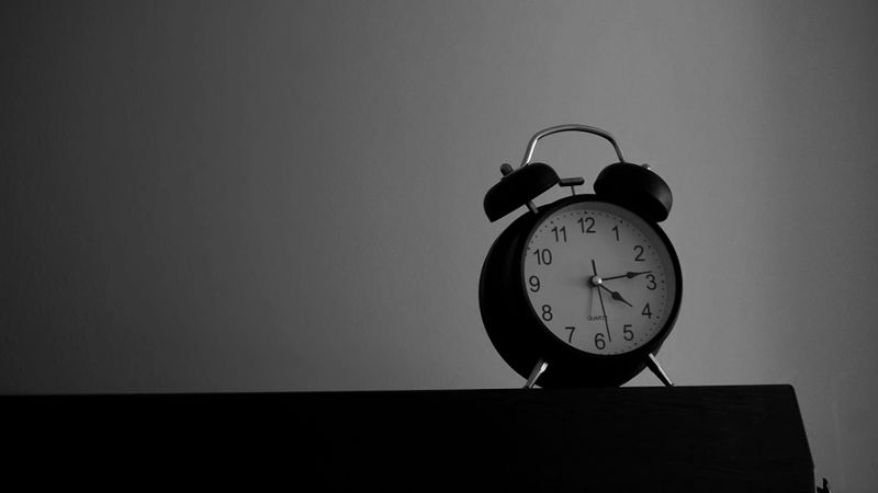 Imagen en blanco y negro de un reloj despertador clásico sobre una superficie oscura, mostrando las 10:10, sobre un fondo liso.