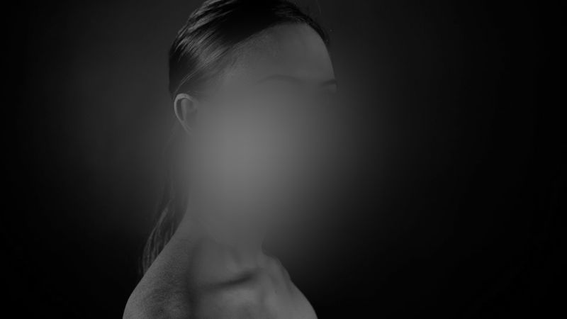 Una imagen en escala de grises de una persona con el rostro difuminado, mostrando un perfil lateral contra un fondo oscuro.