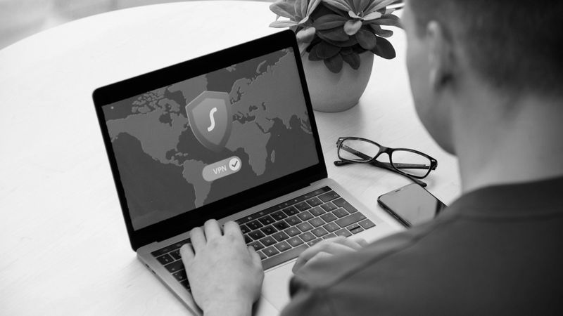 Person, die einen Laptop benutzt, auf dem ein VPN-Bildschirm mit einer Karte angezeigt wird, neben einem Smartphone und einer Brille auf einem Tisch.