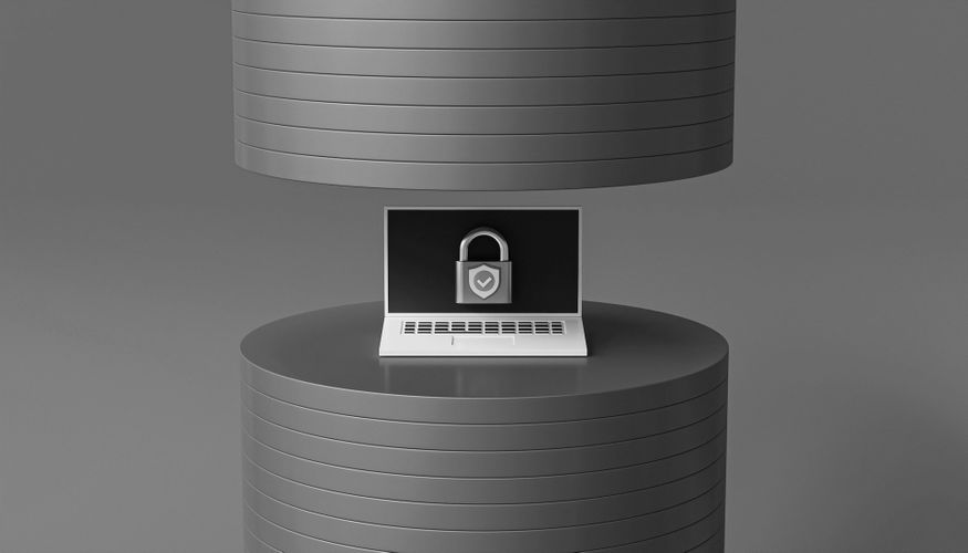 Laptop with a padlock icon on the screen, placed between two large, stacked, cylindrical objects in a monochrome setting.