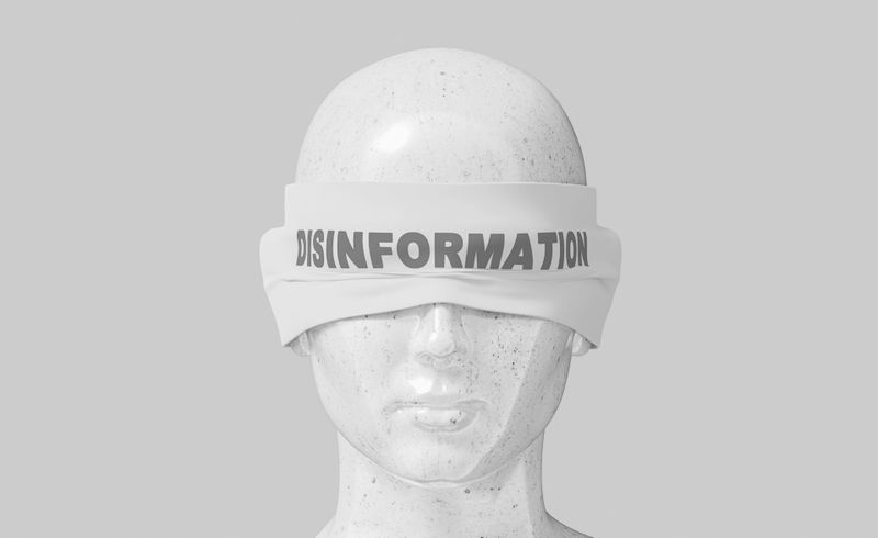 Cabeza de maniquí con una venda en los ojos con la etiqueta "DESINFORMACIÓN" sobre un fondo gris.