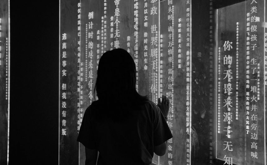 Silhouette d'une personne touchant un mur éclairé avec un texte chinois vertical dans un espace faiblement éclairé.
