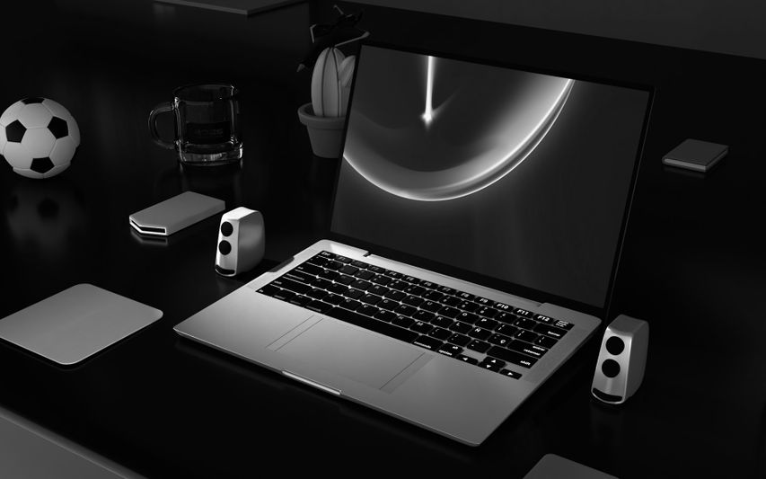Un ordinateur portable élégant sur un bureau sombre, flanqué de petits haut-parleurs, avec un ballon de football, une tasse et une plante en pot en arrière-plan.