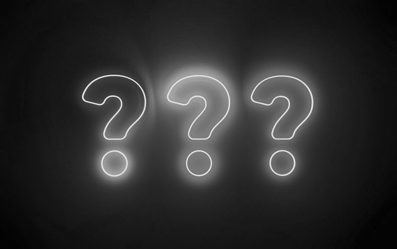 Tres signos de interrogación blancos brillantes sobre un fondo oscuro, espaciados uniformemente y emitiendo una luz suave.