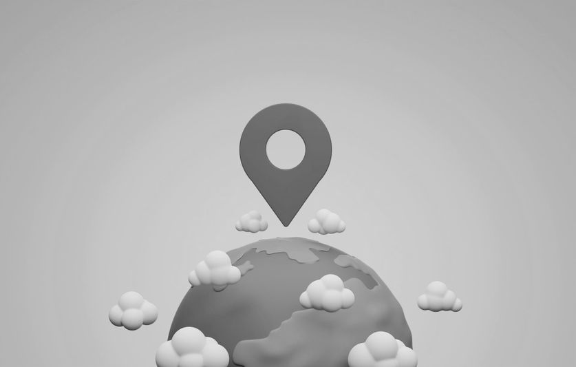 Globe gris avec une épingle de localisation au-dessus, entouré de petits nuages, sur un fond gris clair.