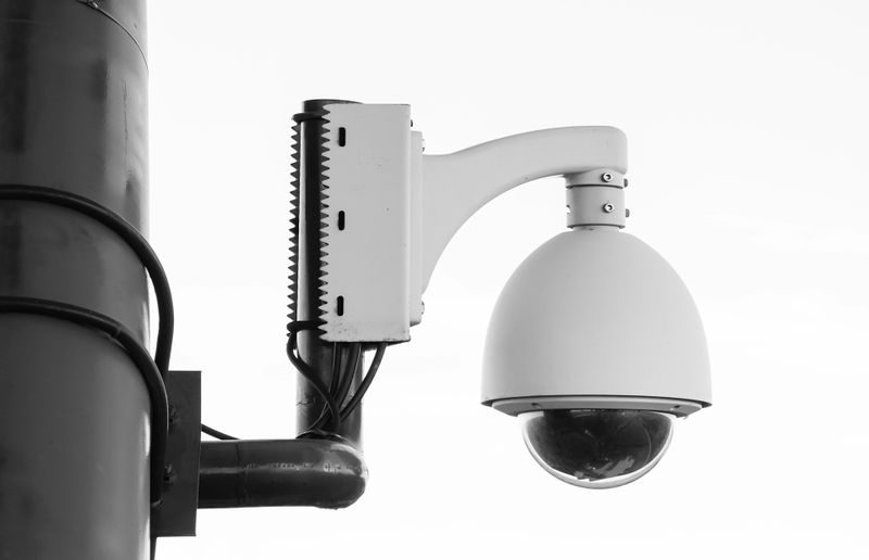 White dome security camera mounted on a pole with metal bracket and visible cables.
