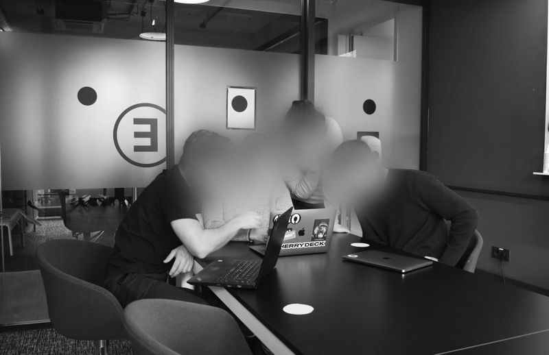 Vier Personen sitzen um einen Tisch mit Laptops in einem modernen Büro und arbeiten gemeinsam an einem Projekt. Ihre Gesichter sind aus Datenschutzgründen verschwommen.