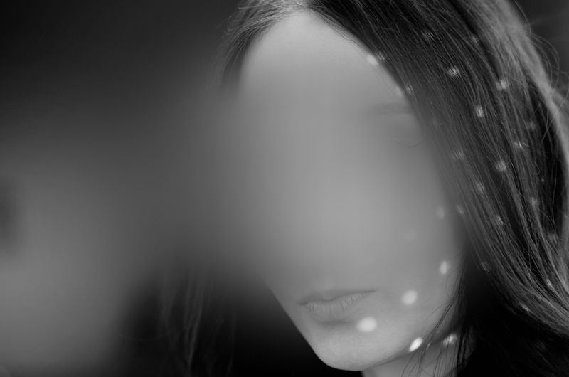 Una imagen en blanco y negro del rostro de una mujer parcialmente oculto por manchas de luz difusas, creando un efecto misterioso y etéreo.