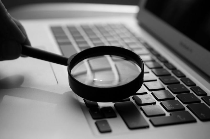 Loupe tenue au-dessus d'un clavier d'ordinateur portable, focalisant sur les touches. L'image est en noir et blanc, mettant en valeur les détails et la texture.