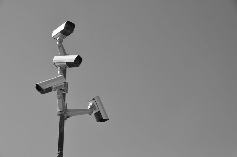 A cluster of security cameras mounted on a pole against a clear sky, captured in black and white.